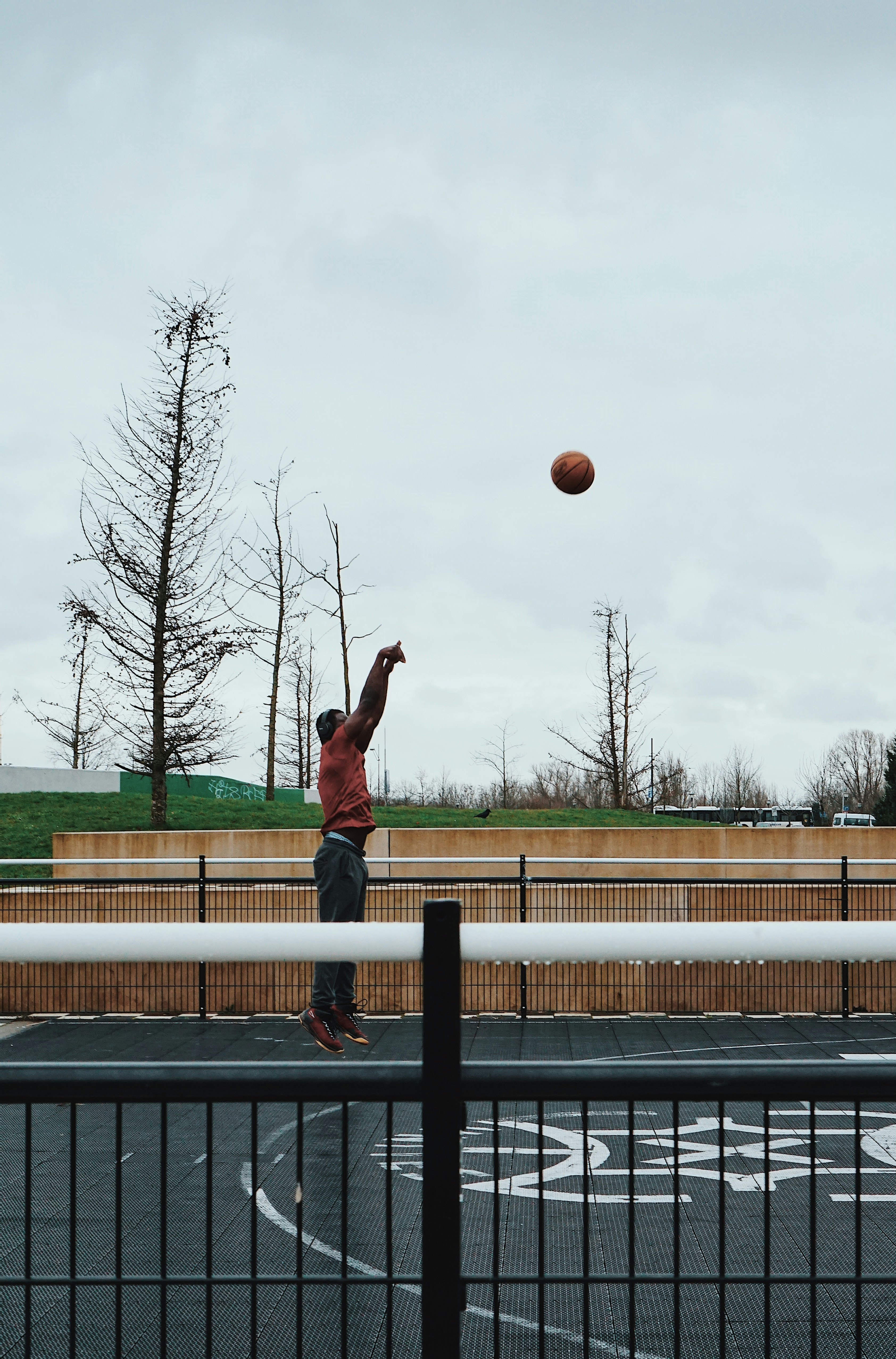 man in black tank top and brown shorts jumping on brown wooden fence during daytime